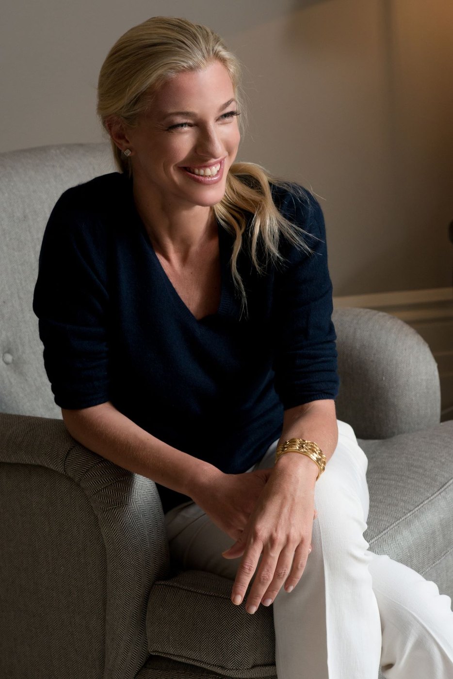 Nicole Junkermann smiling as she sits in a pale armchair, a relaxed portrait