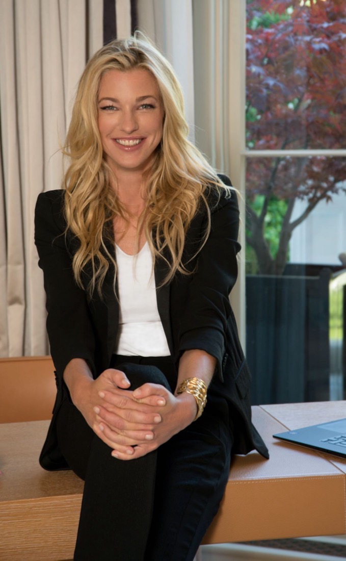 Retrato de Nicole Junkermann con blazer negro sonriendo, sentada en un escritorio junto a una ventana